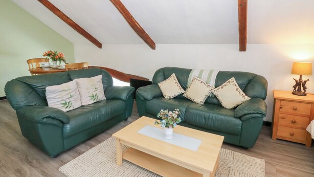 A cozy living room with two green leather sofas, a wooden coffee table, and a small wooden side table with a lamp. - Loft Apartment (Llandysul)