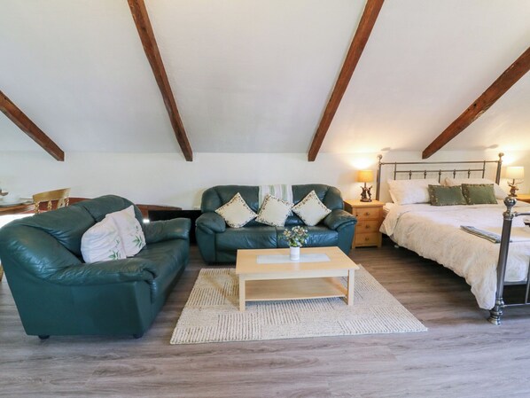 A cozy room with two green leather sofas, a wooden coffee table, and a bed with a white duvet. - Loft Apartment (Llandysul)