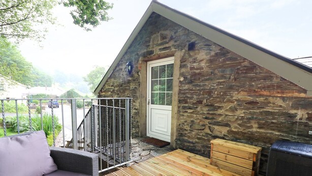 En byggnad med tak av sten, en träveranda, en vit dörr och en soffa av rotting.
