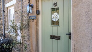 A green door with a glass panel, a sign reading "Teal Cottage," and a potted plant beside a table. - Teal Cottage (Leyburn)