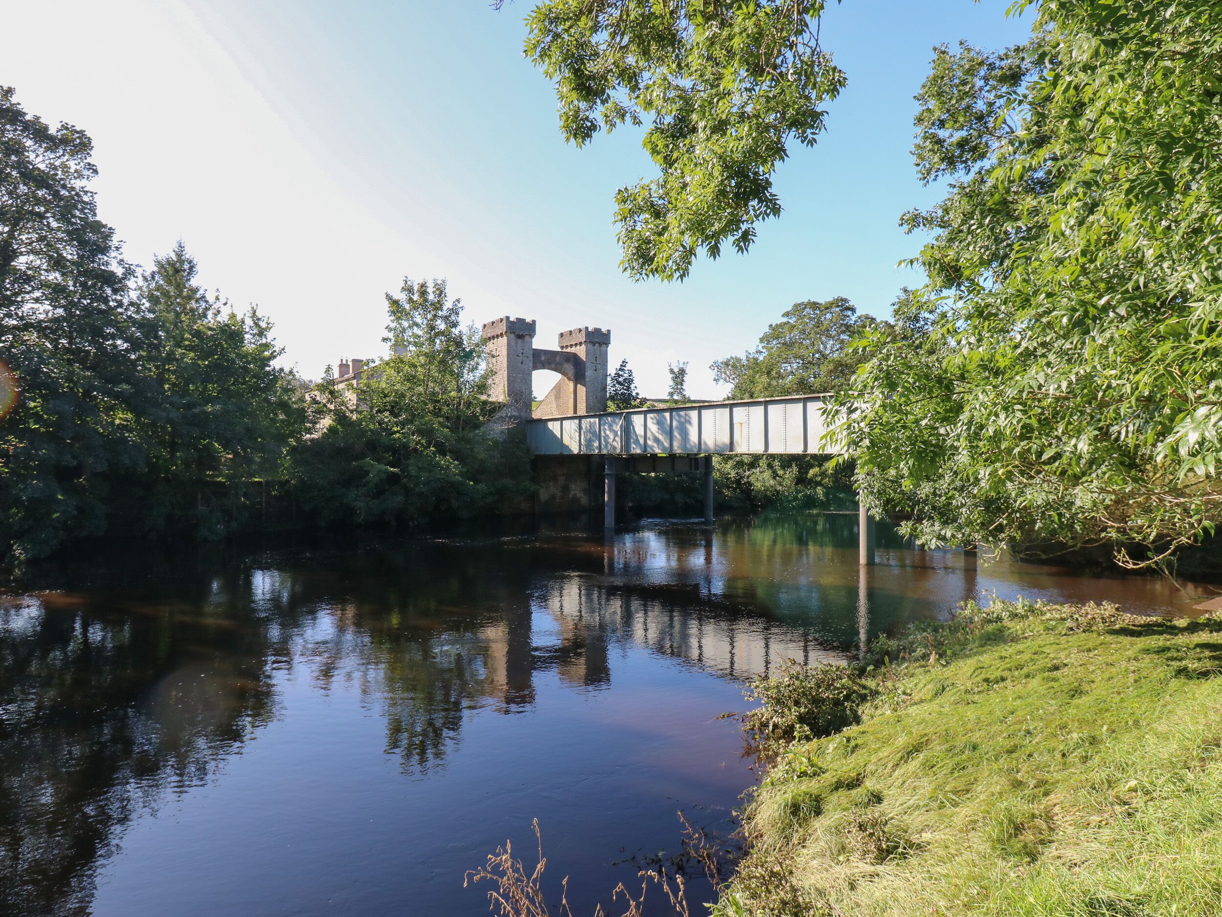 A river with a bridge, surrounded by greenery and a castle-like structure in the background.