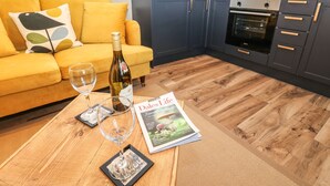 A modern kitchen with a microwave, oven, and dark cabinets. A bottle of wine and two glasses are on a wooden table. - Teal Cottage (Leyburn)