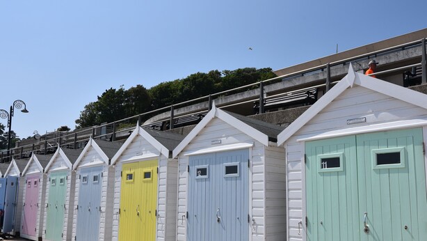 A row of colorful beach huts with numbered doors, a staircase, and a clear sky.
