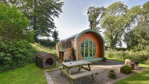 A wooden hobbit house with a round door, a picnic table, and a rustic outdoor setting.