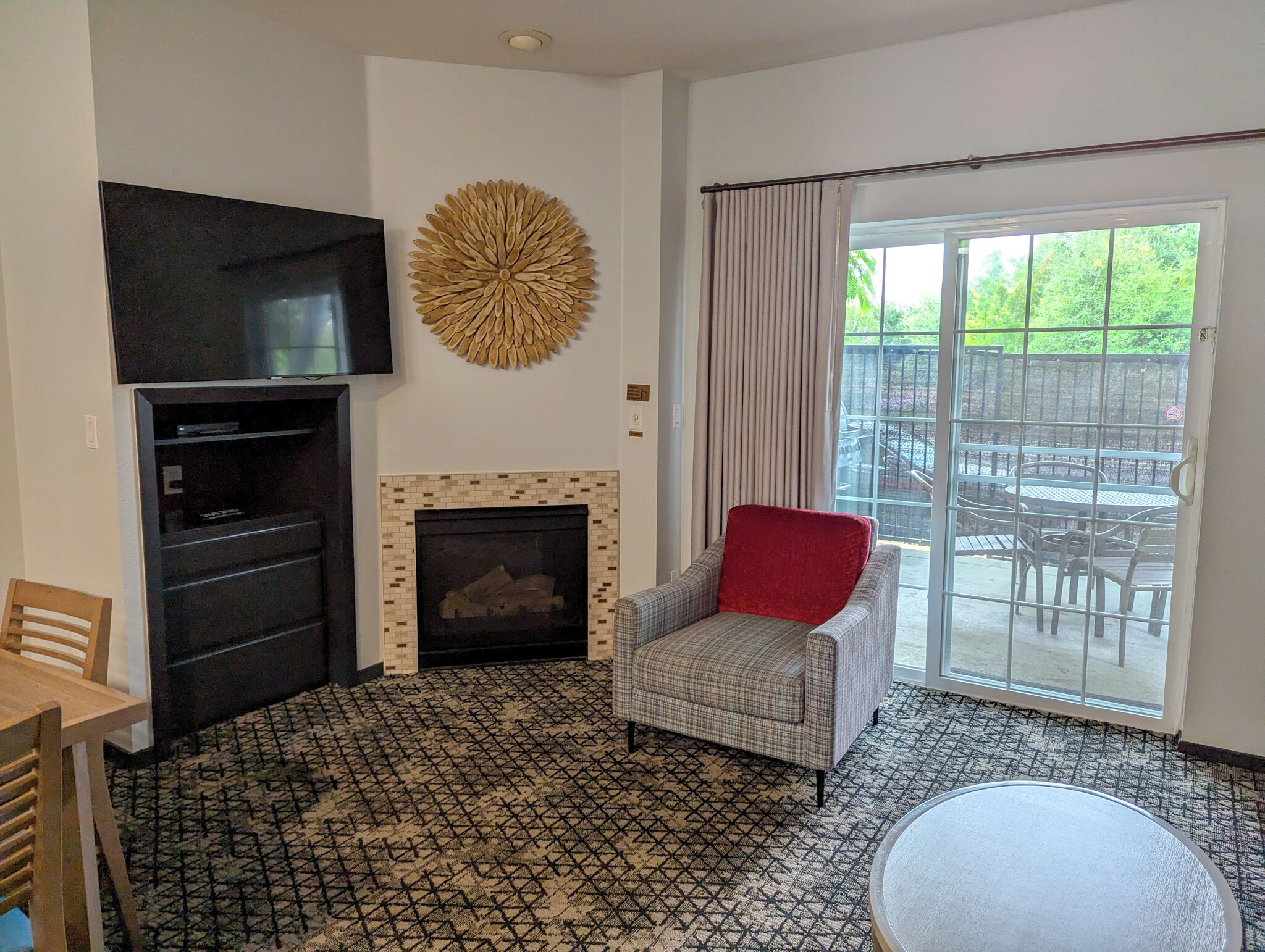 Un salon avec une cheminée, un téléviseur, un fauteuil rouge et une vue sur une terrasse extérieure.