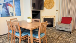 A dining area with a wooden table and blue cushioned chairs, a flat-screen TV mounted above, a decorative wall piece, and a fireplace with a tiled surround. - 3BR: Danish-Style Retreat in CA Wine Country (Solvang)