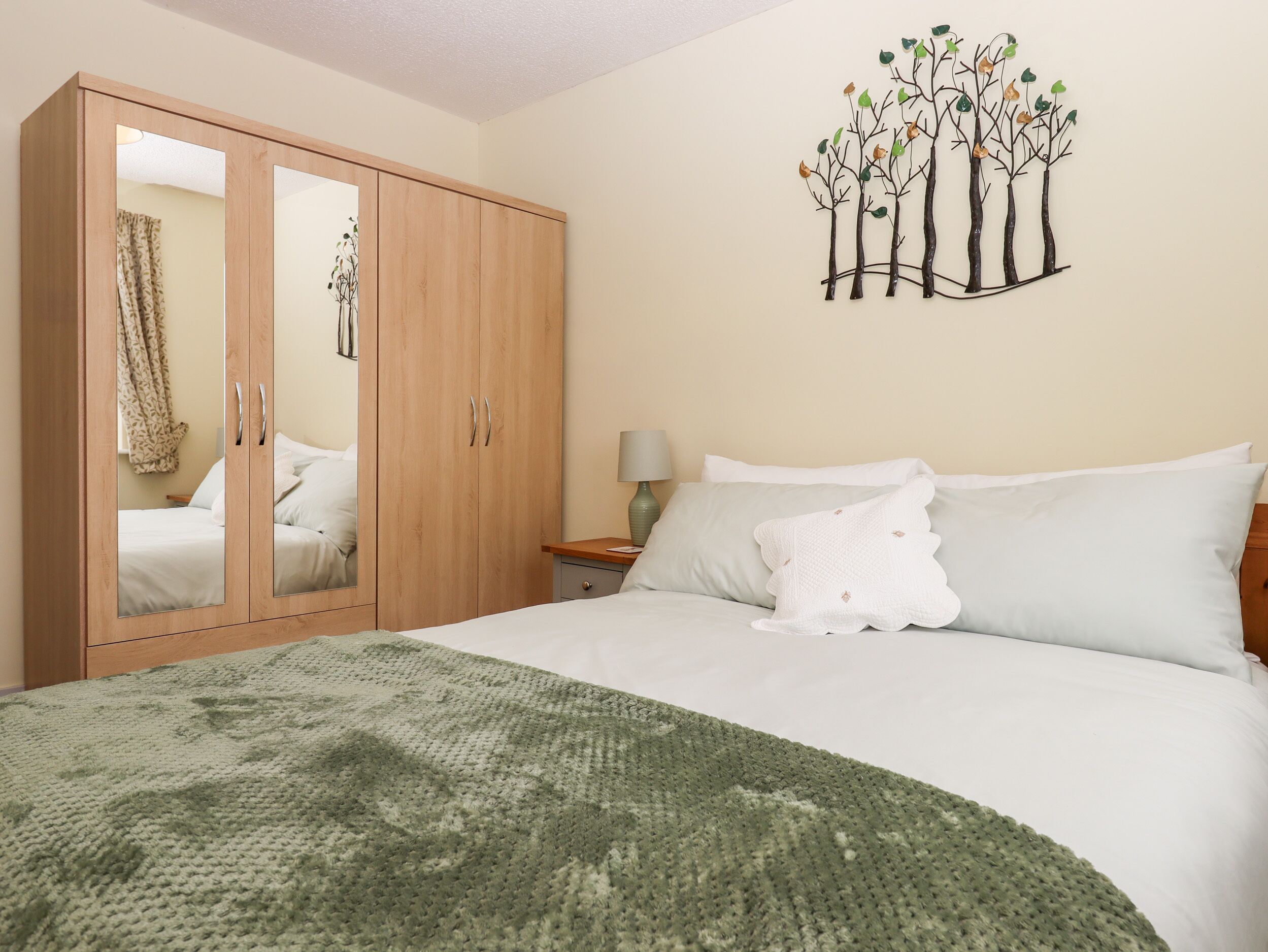 A bedroom with a bed, a wardrobe, a nightstand, a lamp, and a wall art piece.