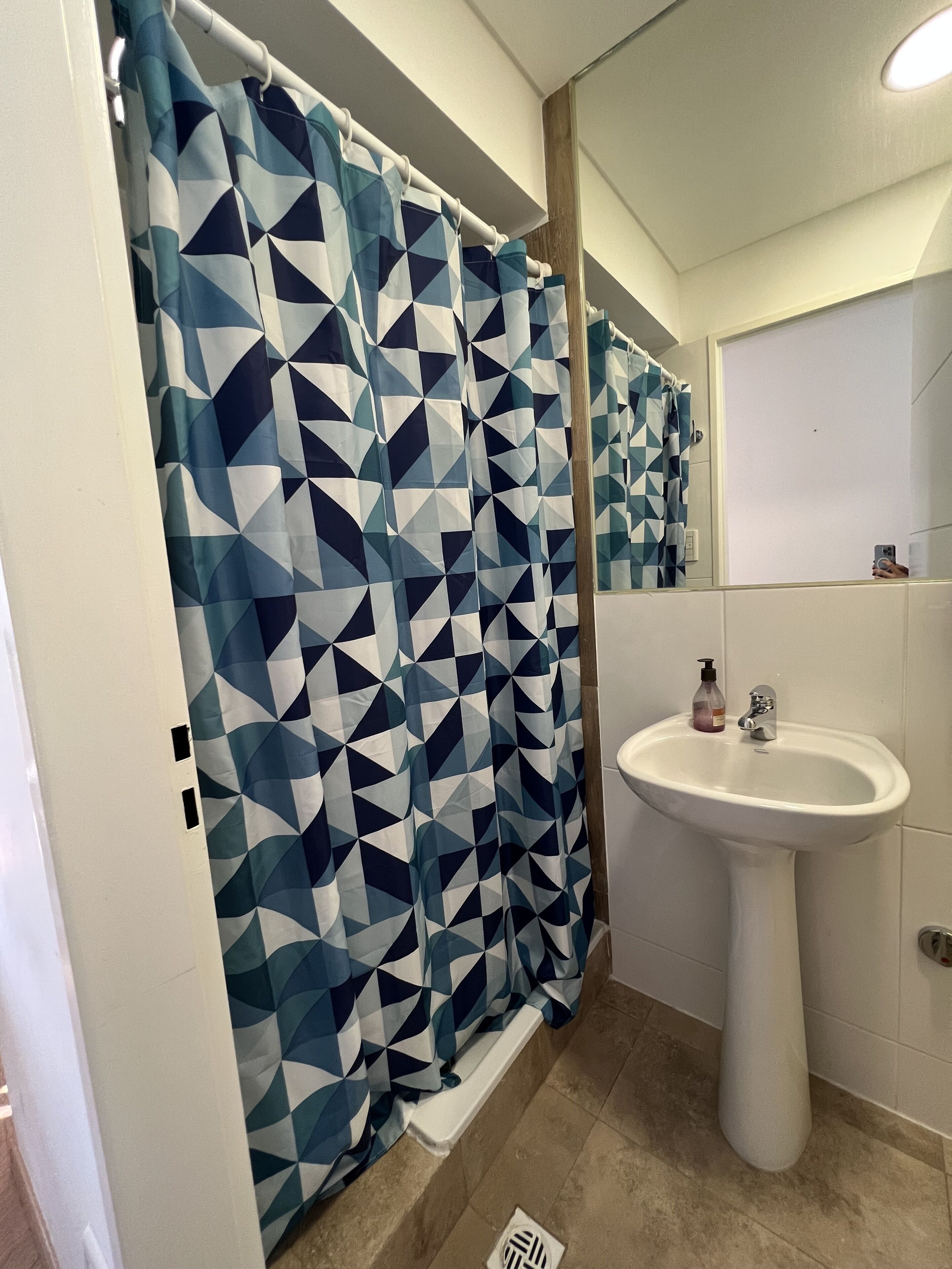 A bathroom with a geometric patterned shower curtain, a white pedestal sink, and a mirror above it.