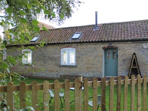 A stone building with a tiled roof, a green door, and a wooden fence. - Swallow's Nest (Gainsborough)