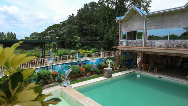 A swimming pool area with a house in the background, surrounded by greenery and a decorative fence. - Villa Elsie Resort and Hotel (General Trias)