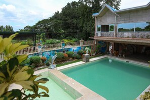 A swimming pool area with a house in the background, surrounded by greenery and a decorative fence. - Villa Elsie Resort and Hotel (General Trias)