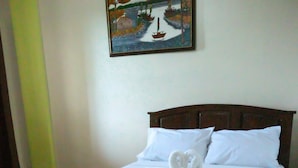 A neatly made bed with white linens and two towels arranged in a swan shape, a wooden headboard, and a painting of a tropical scene on the wall. - Villa Elsie Resort and Hotel (General Trias)