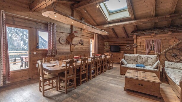 Interior de una cabaña de madera con comedor, sofá y televisor.