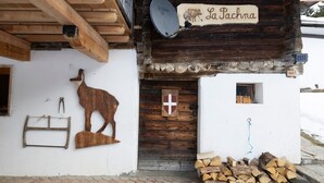 Un edificio rústico con fachada de madera, una cabeza de animal montada, una escalera de madera, una antena parabólica y un letrero que dice 'La Pachma'.