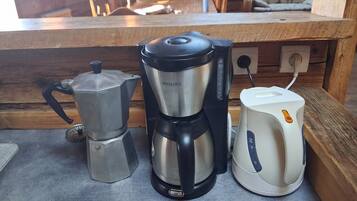A kitchen counter with a coffee maker, a coffee pot, and a kettle.