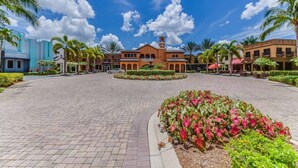 A hotel courtyard with a central fountain, palm trees, and a mix of modern and traditional architecture. - 8209 Bibiana Way 403 (Fort Myers)