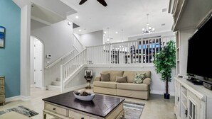 A spacious living room with a beige sofa, a coffee table, and a staircase leading to an upper level. - 8209 Bibiana Way 403 (Fort Myers)