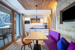 A modern kitchen with a wooden ceiling, a dining area with a table and chairs, and a large window overlooking a snowy landscape.