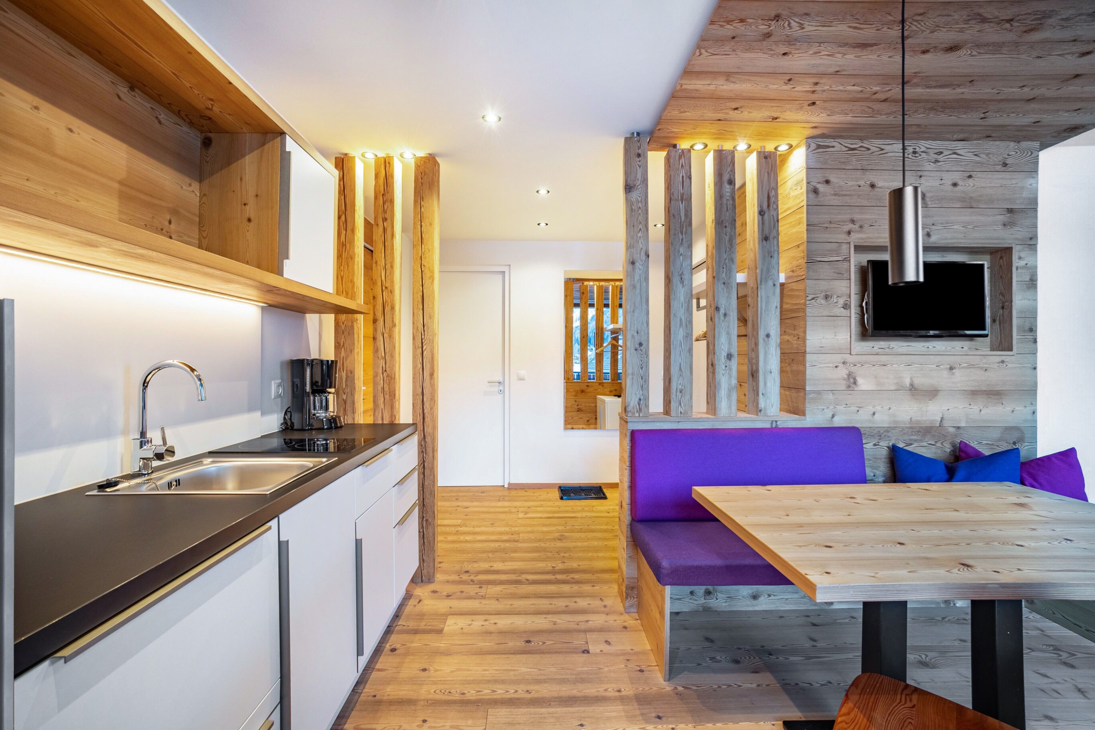 Een moderne keuken met houten plafond, een ingebouwde televisie en een eethoek met een houten tafel en paarse zittingen.