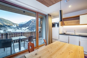 Une cuisine moderne dotée d’une grande fenêtre, d’une table à manger et offrant une vue sur un paysage montagneux enneigé.
