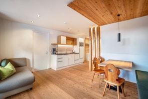 A modern living space with a sofa, dining table, chairs, and a kitchen area.