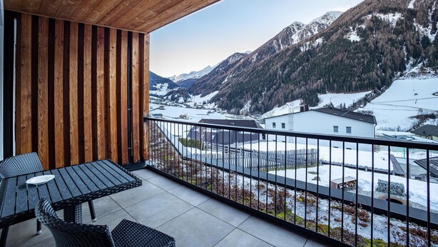 A balcony with a wooden ceiling, a table with chairs, and a view of snow-covered mountains. - Holiday Apartment "Stoana 2-2" with Relaxing Wellness Area (Valle Aurina)