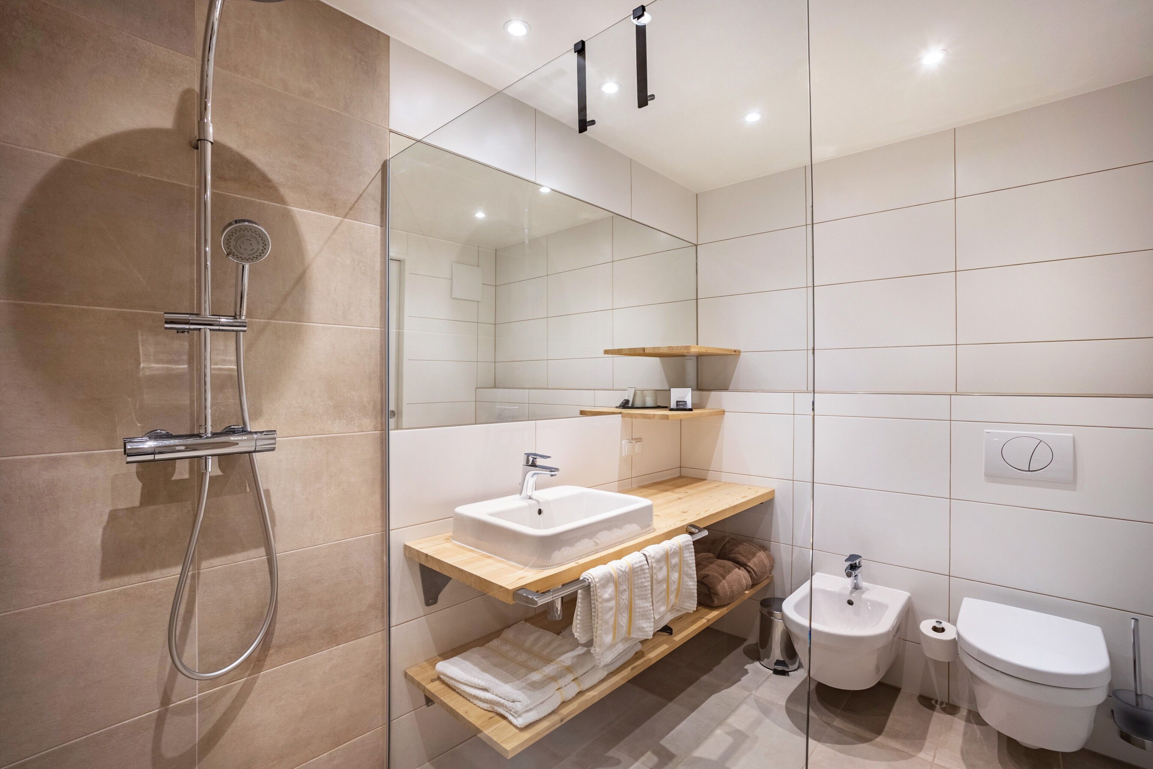 Un baño moderno con cabina de ducha de vidrio, un lavamanos blanco, un bidé y un inodoro.