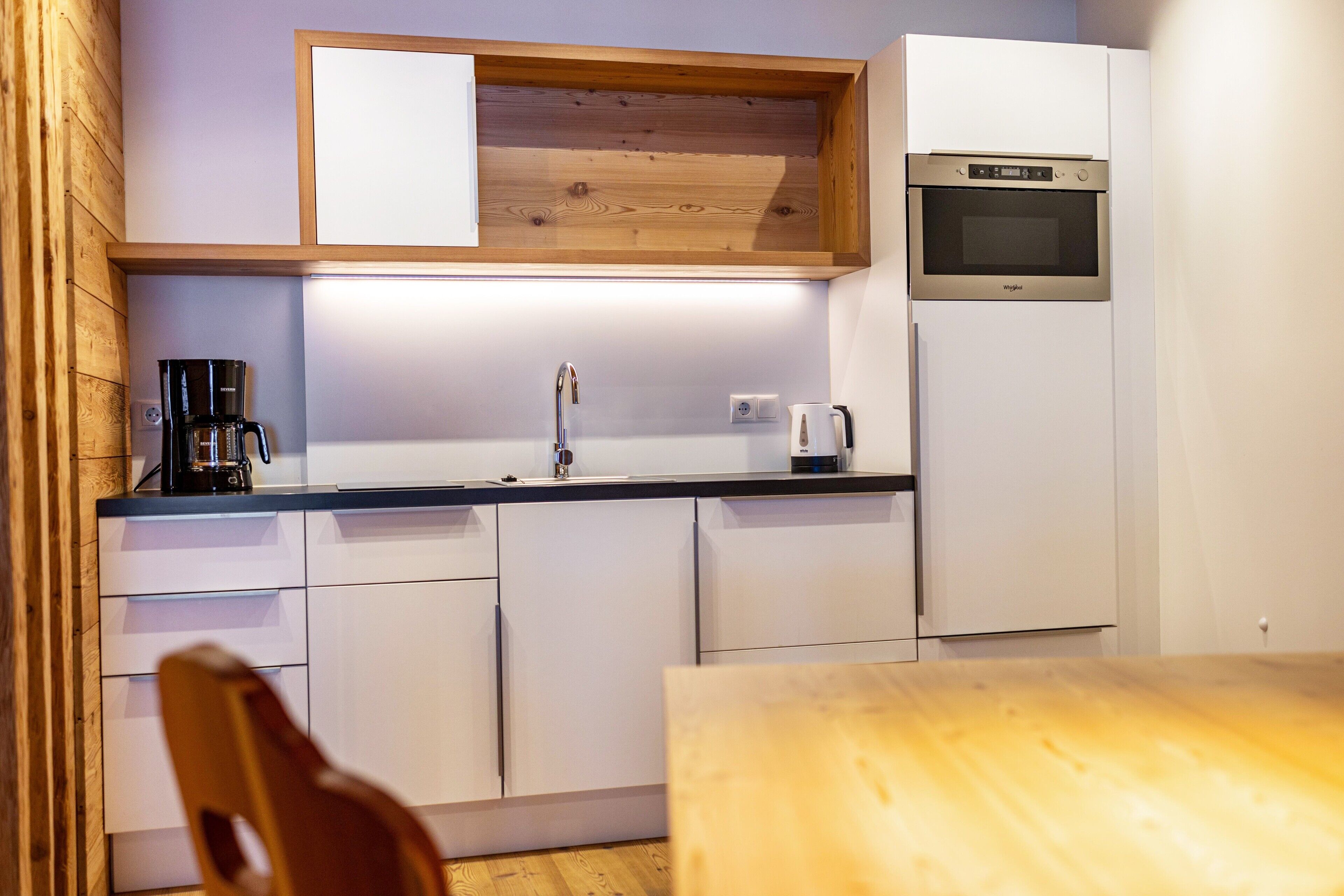Une cuisine compacte avec des meubles blancs, un plan de travail en bois, un four encastré et une machine à café.