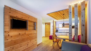 Et moderne interiør med træpaneler, et fladskærms-tv på væggen, et spiseområde med bord og stole, og et køkkenområde med træbjælker i loftet.