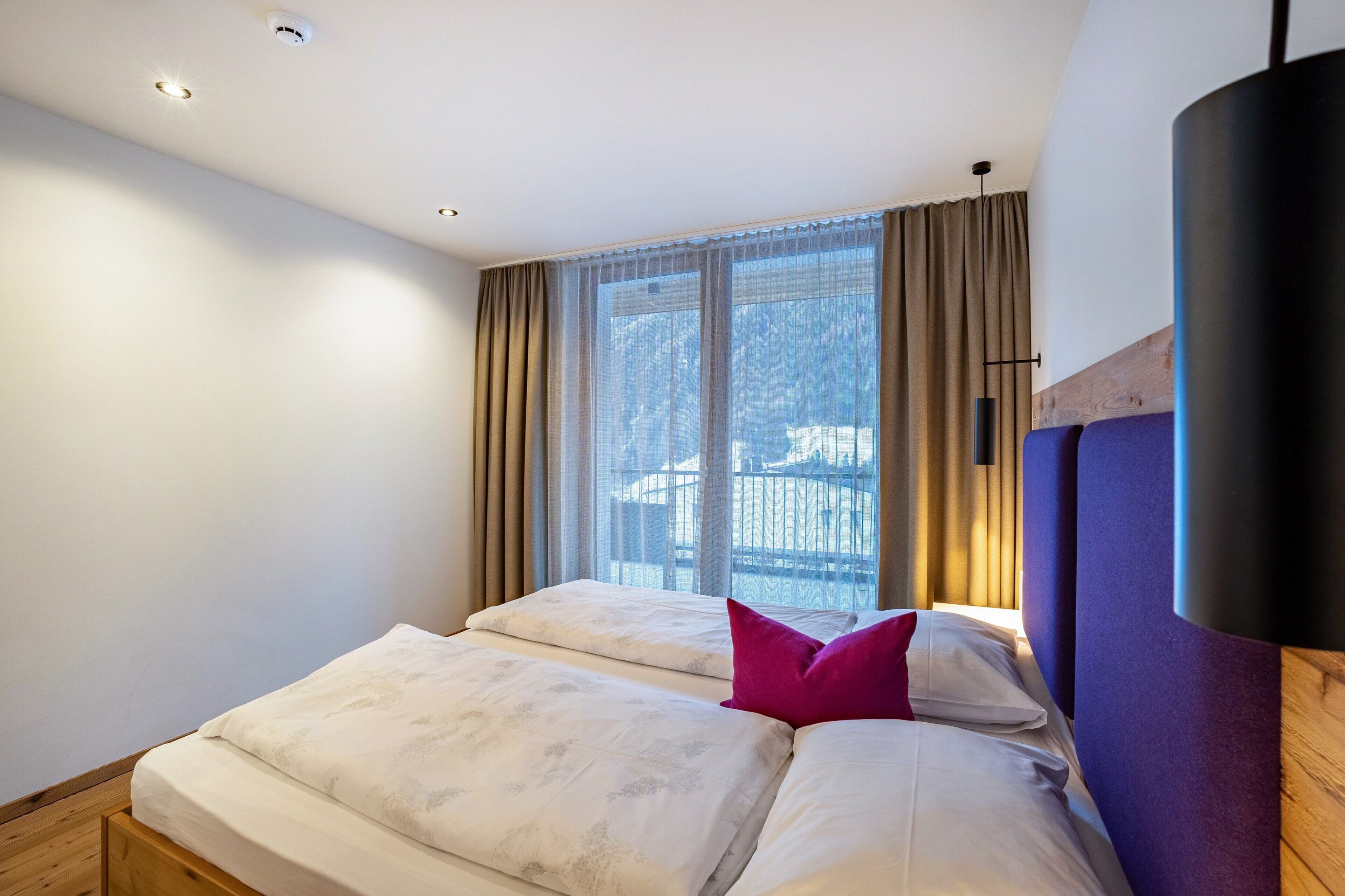 A bedroom with a bed, a window with curtains, and a ceiling light.
