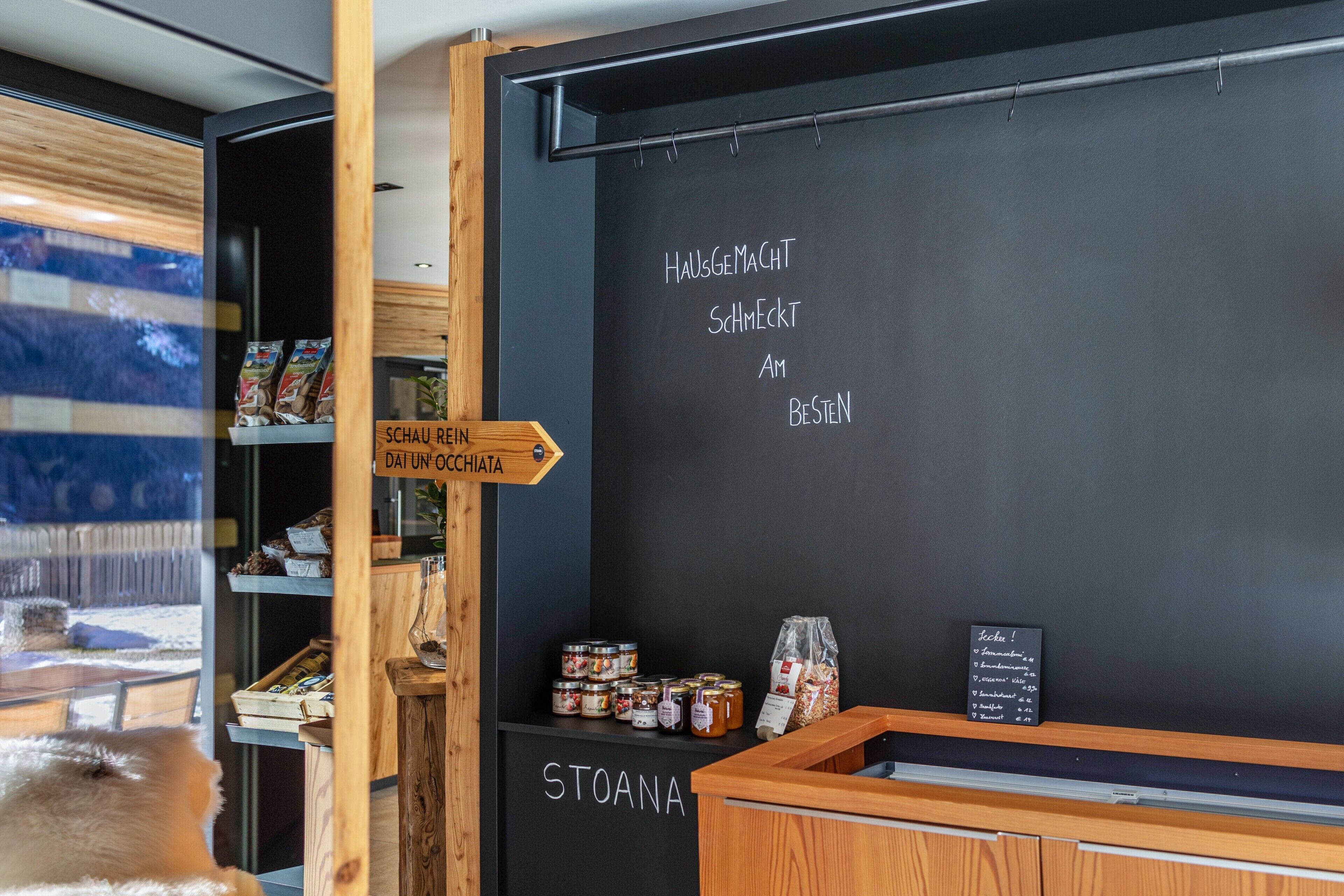 A blackboard with text, wooden shelves with products, and a window view.