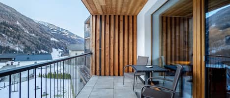 A balcony with a wooden ceiling, a glass door, and a view of a snowy mountain.
