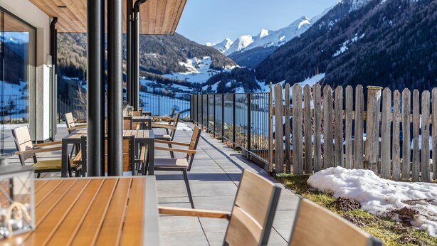 An outdoor seating area with tables and chairs, a wooden fence, and a view of snow-capped mountains.