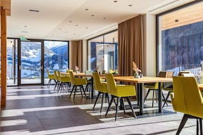 Una hall d'albergo moderna con ampie finestre, sedie gialle e un tavolo in legno.