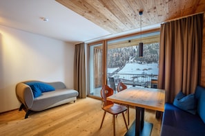 Un interno moderno con soffitto in legno, un divano, un tavolo da pranzo con sedie e un'ampia finestra con vista sulle montagne innevate.