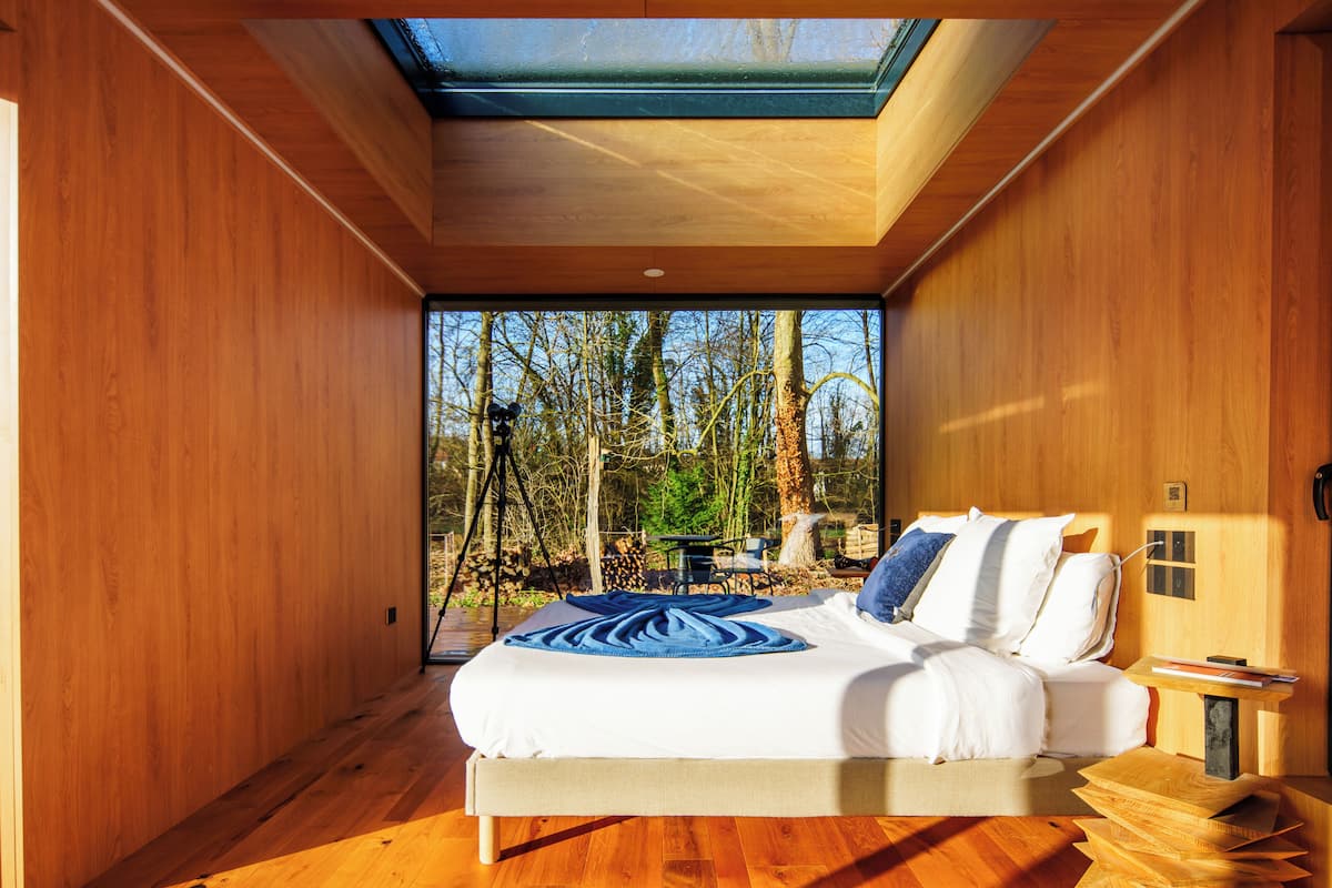 Ein modernes Schlafzimmer mit Dachfenster, einem Bett mit weißen Bettwäsche und Blick auf Bäume.