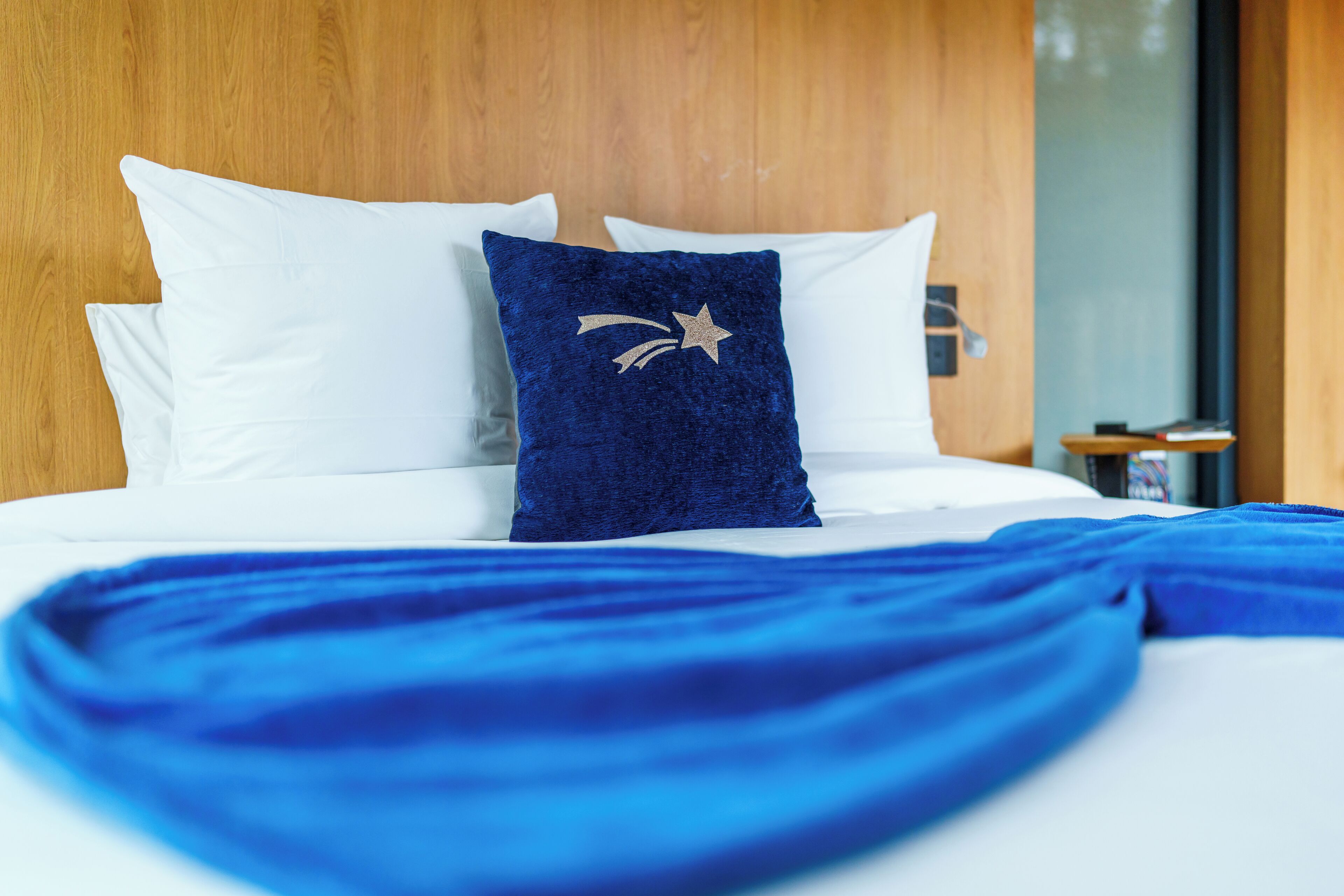 Una cama con ropa de cama blanca y azul, un cabecero de madera y un cojín decorativo con un diseño de estrella.
