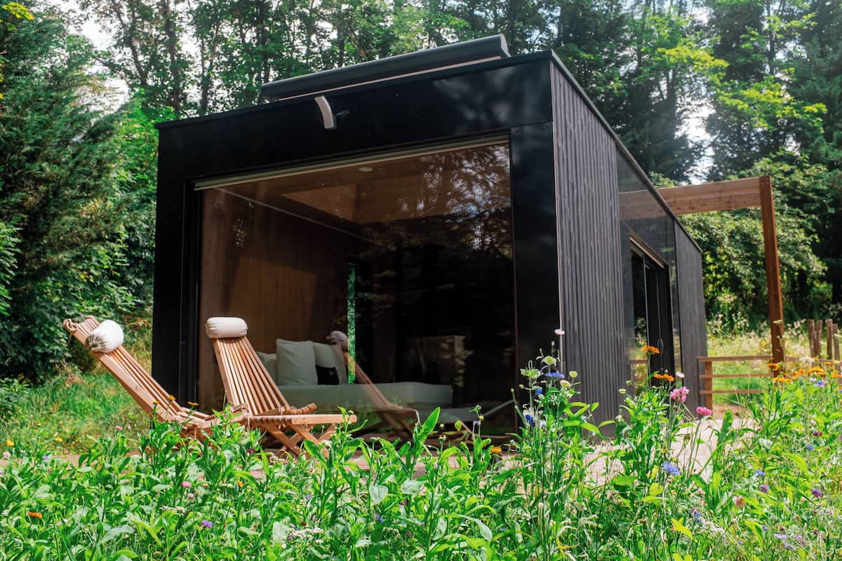 Eine moderne, kompakte Holzhütte mit Glastür, einer Holzterrasse und einer Hängematte.