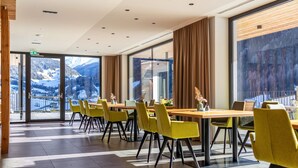 A modern hotel lobby with large windows, yellow chairs, and a wooden table.