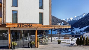 A hotel named STOANA with a mountain view, large windows, and a covered outdoor seating area.