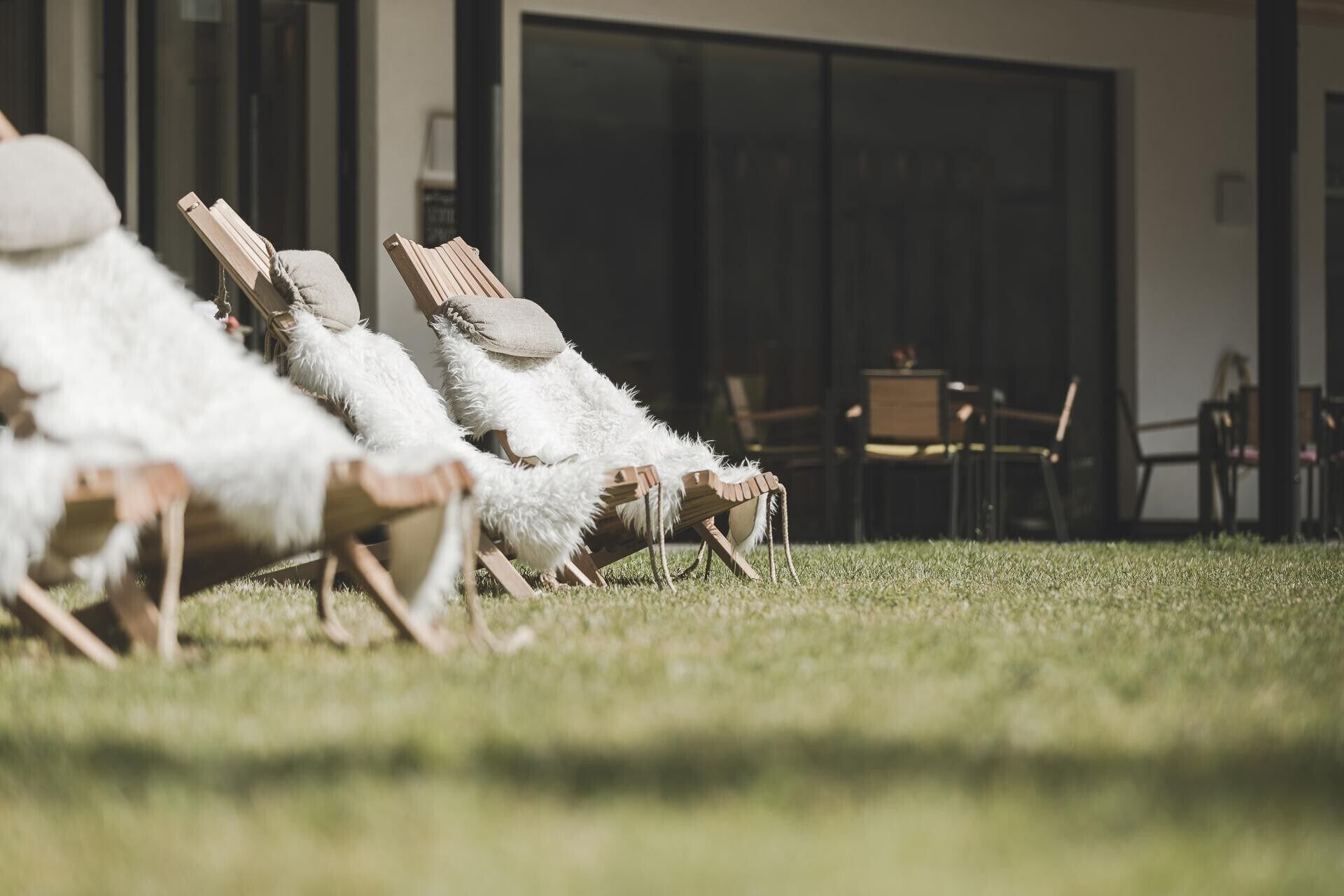 Outdoor lounge chairs with a grassy area, a building entrance, and a seating area inside.
