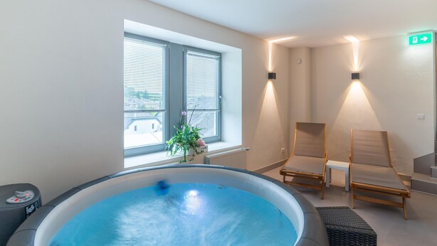 Un cuarto de spa con un jacuzzi, dos sillas de madera, una ventana con persianas e iluminación empotrada.