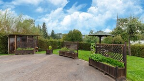 Un jardín con jardineras de madera, un pabellón y una zona cubierta.