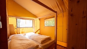 A cozy wooden room with a bed, two windows, and a wooden ceiling.