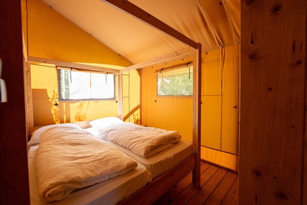 A cozy wooden room with a bed, two windows, and a wooden ceiling.