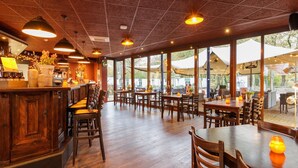 A restaurant with wooden tables and chairs, a bar area, and large windows allowing natural light.