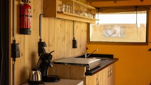 A kitchen with wooden cabinets, a coffee maker, a kettle, a fire extinguisher, and a window with a view.