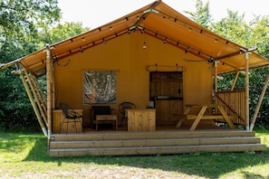A wooden cabin with a covered porch, a dining table, chairs, and a large painting on the wall.