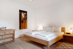 Quarto com cama de madeira, cômoda, pintura pendurada na parede, abajures e tapete.