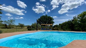 A swimming pool with a tiled deck, surrounded by trees and a clear sky. - Farmhouse "Gufo" with Shared Pool, Private Terrace & Wi-Fi (Pitigliano)